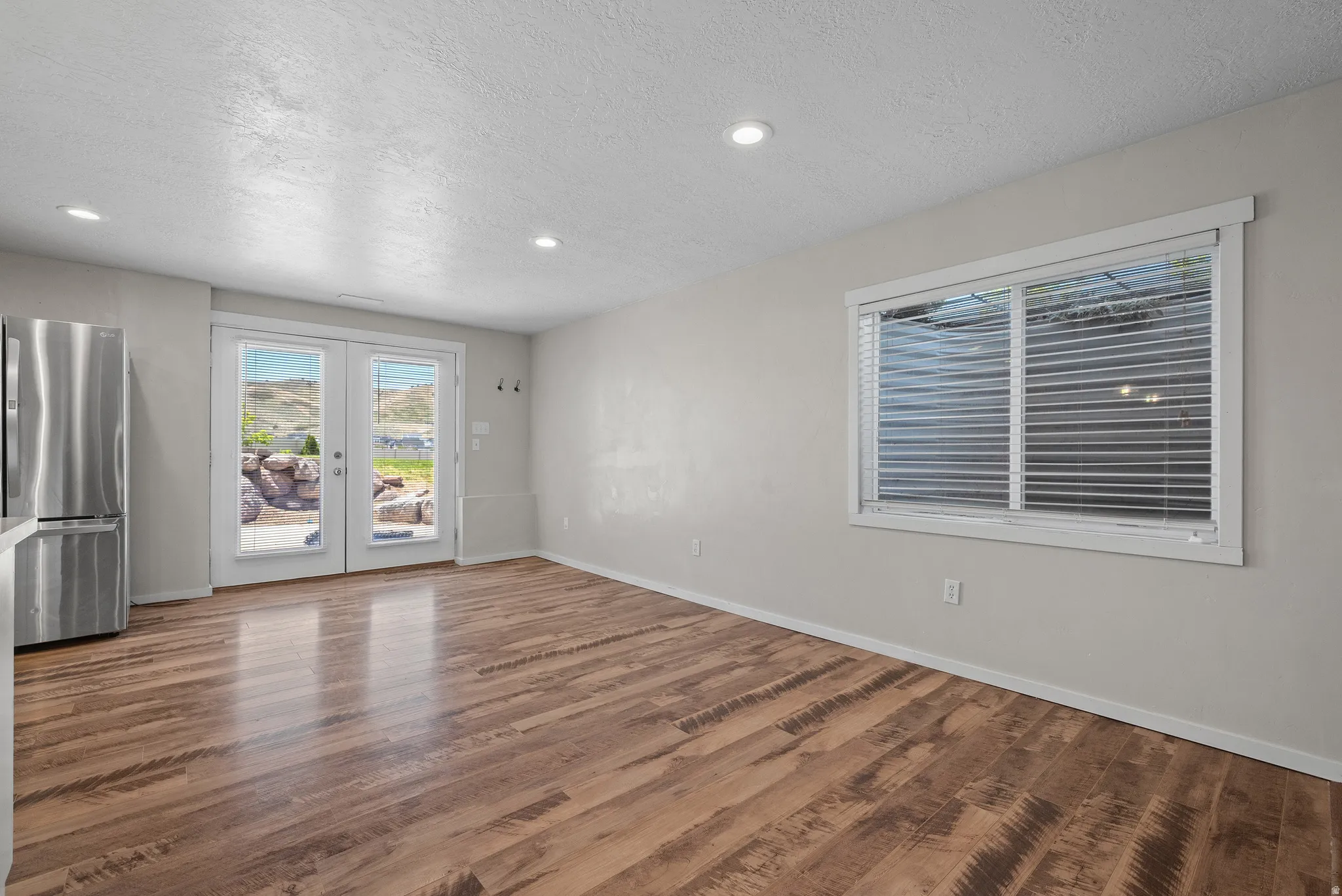 Spacious area featuring wood-finish flooring, recessed lighting, and a stainless steel refrigerator
