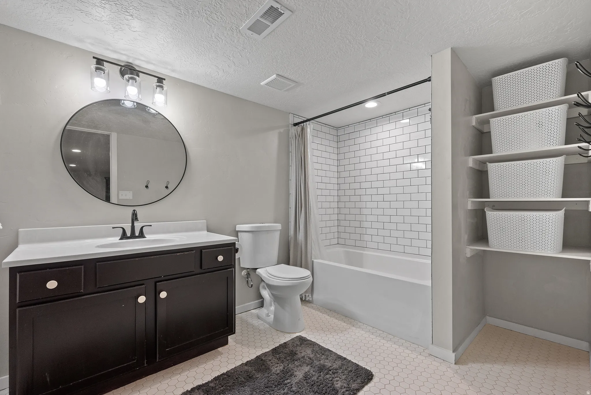 Bathroom featuring a dark wood-finish vanity with a white countertop and round mirror, white subway tile shower surround, and built-in shelving