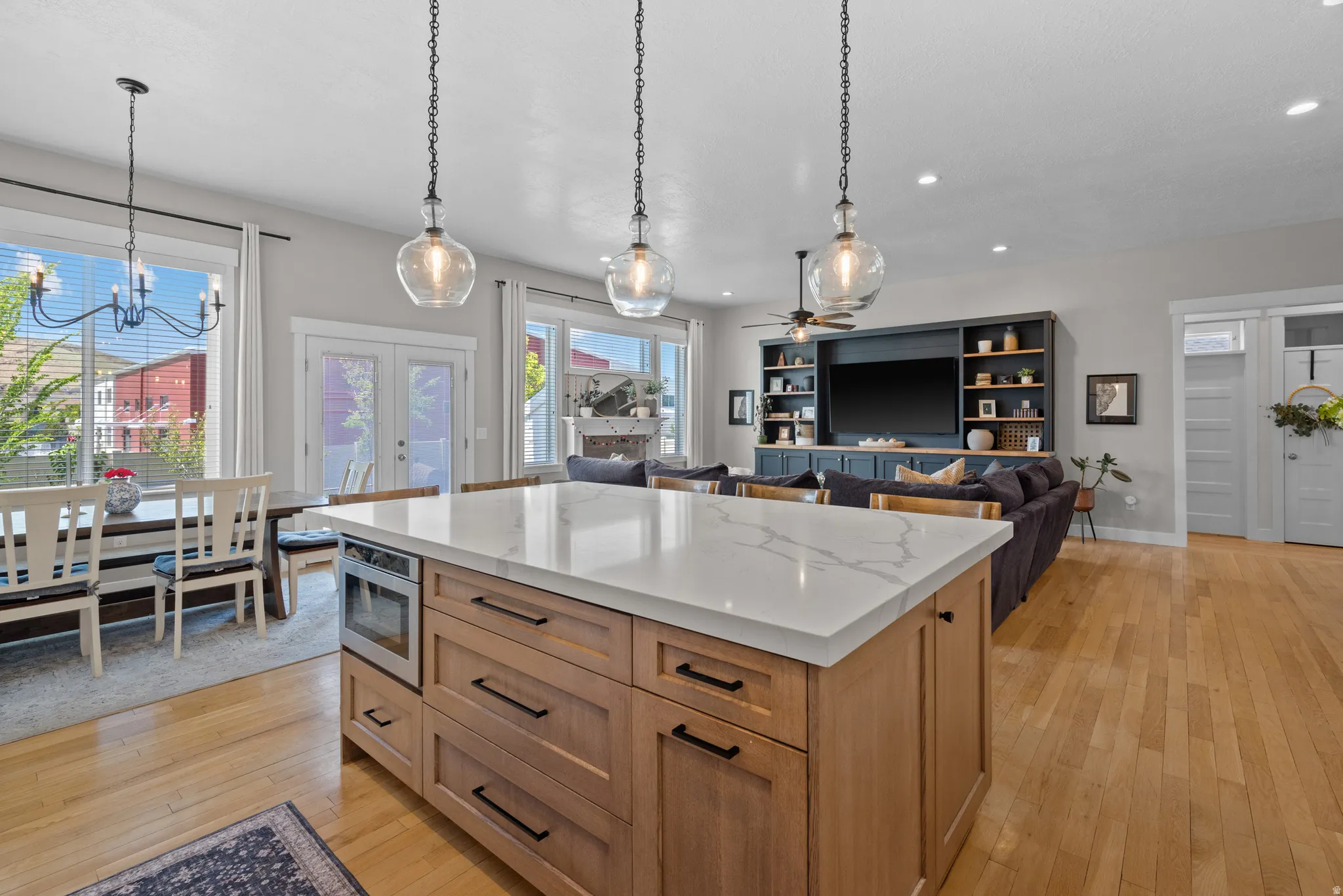 Spacious open-concept living area featuring a large kitchen island with a light-toned countertop, hardwood flooring, built-in shelving, and recessed lighting