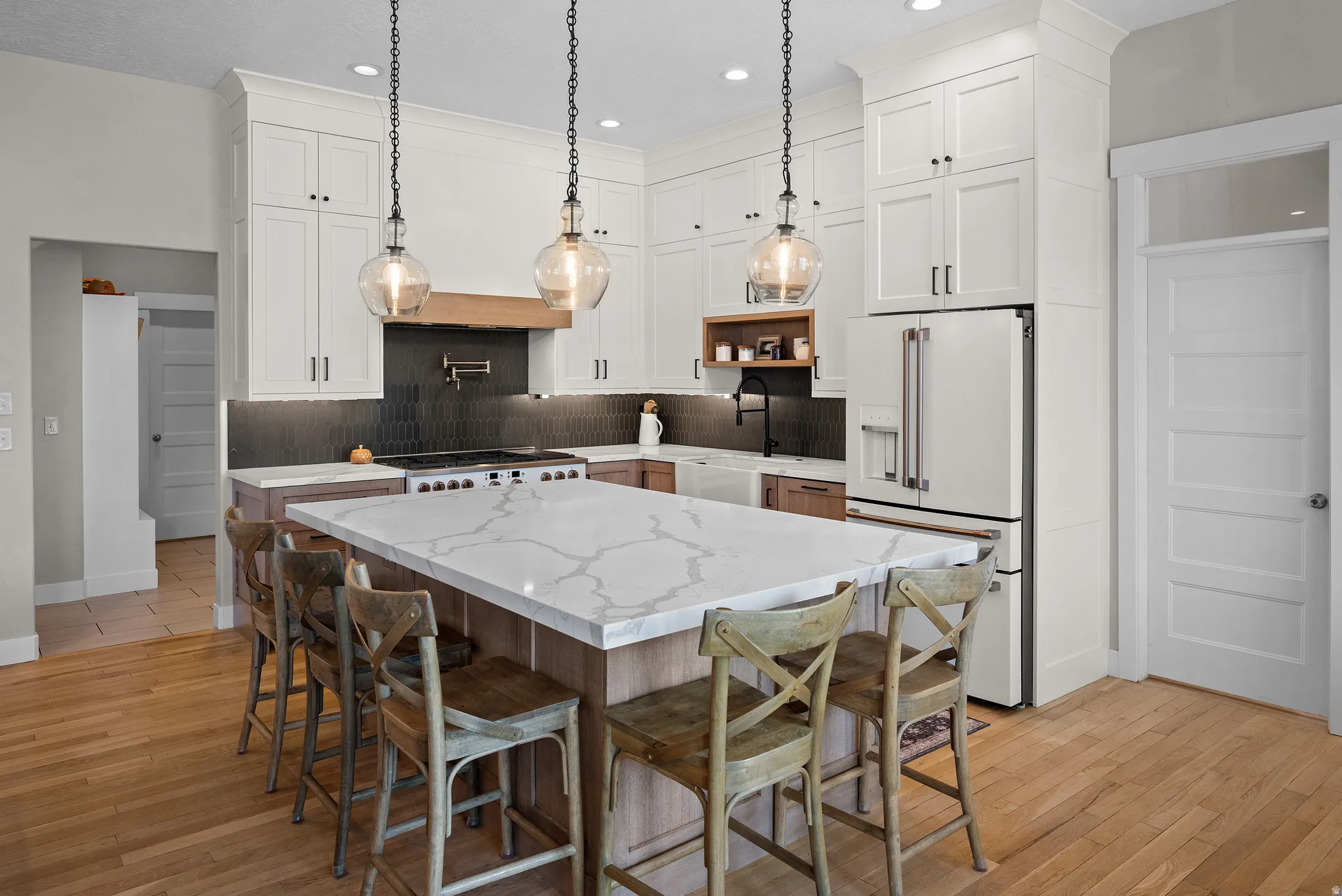 Central kitchen island with a white veined countertop, pendant lighting, professional-grade range with pot filler, full-height white cabinetry, and wood-finish flooring