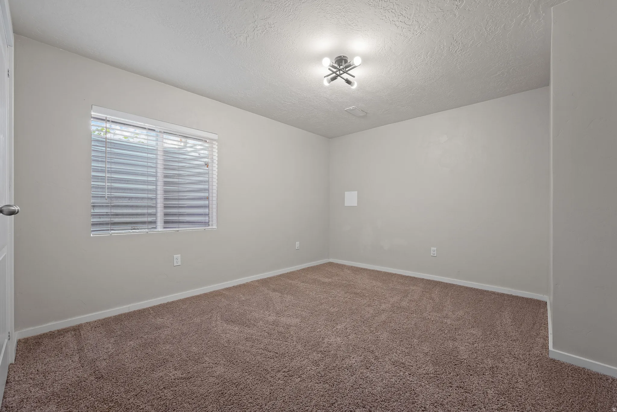 Spacious room featuring neutral paint, brown carpet flooring, a window with horizontal blinds, and a contemporary ceiling light fixture