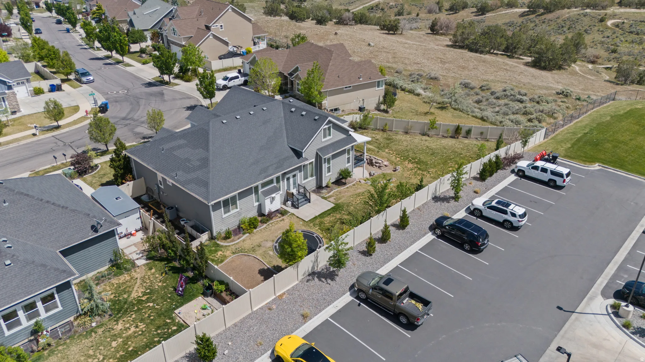 Contemporary-style residence featuring a dark gray roof, light gray siding, and a fenced yard with established landscaping
