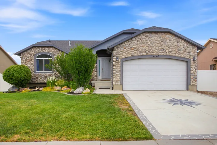 Stone veneer exterior featuring an arched window, a two-car garage with an architectural star detail on the driveway, and a front entry with steps