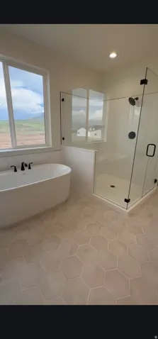 Contemporary bathroom featuring a freestanding soaking tub with matte black fixtures, a spacious glass-enclosed shower with a bench, and hexagonal tile flooring
