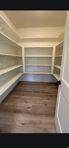Walk-in pantry featuring extensive built-in shelving, wood-finish flooring, and a white paneled door with matte black hardware