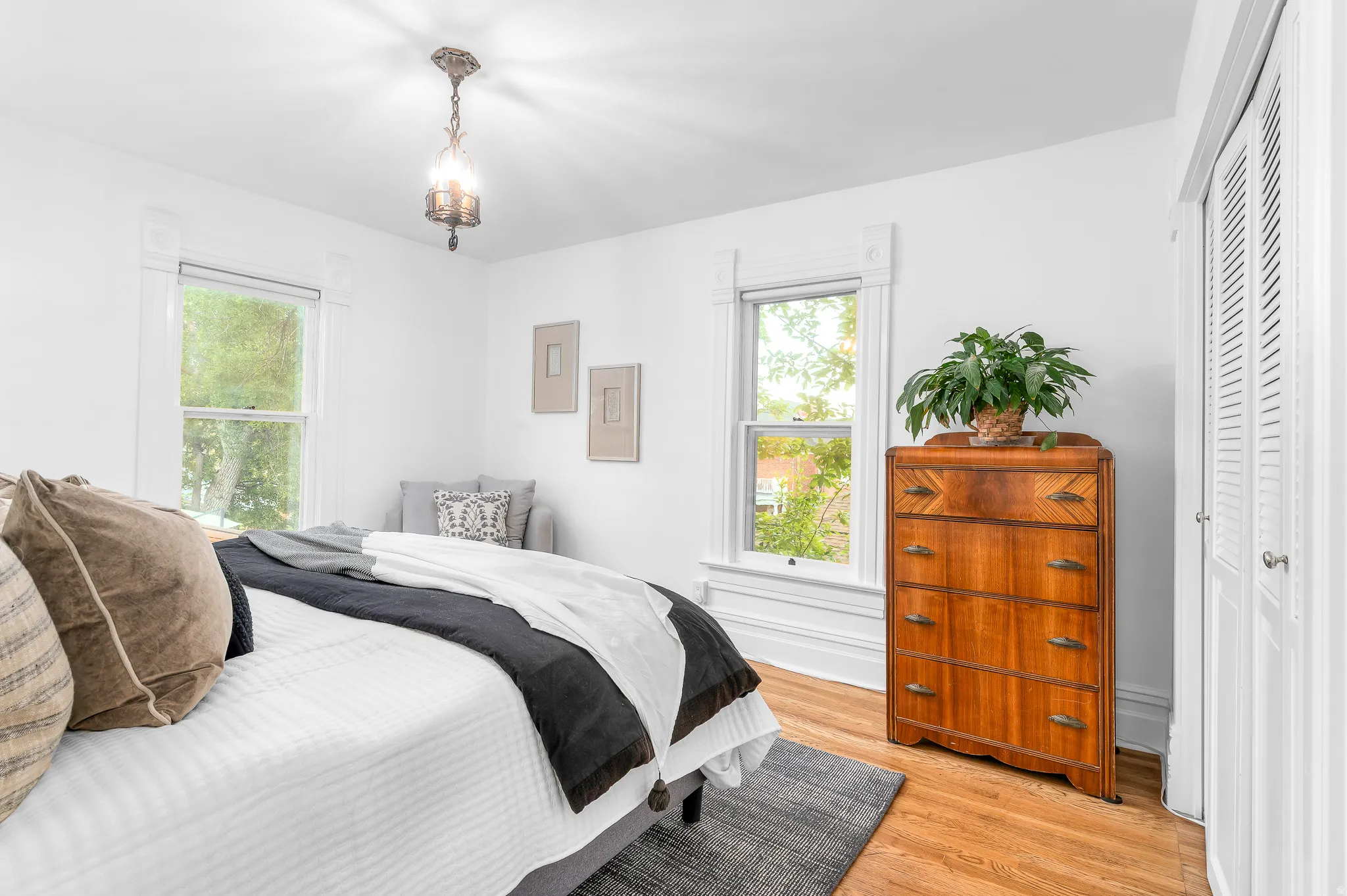 Wood-finish flooring accentuates this room featuring white walls, two large windows with decorative trim, and a prominent bi-fold closet
