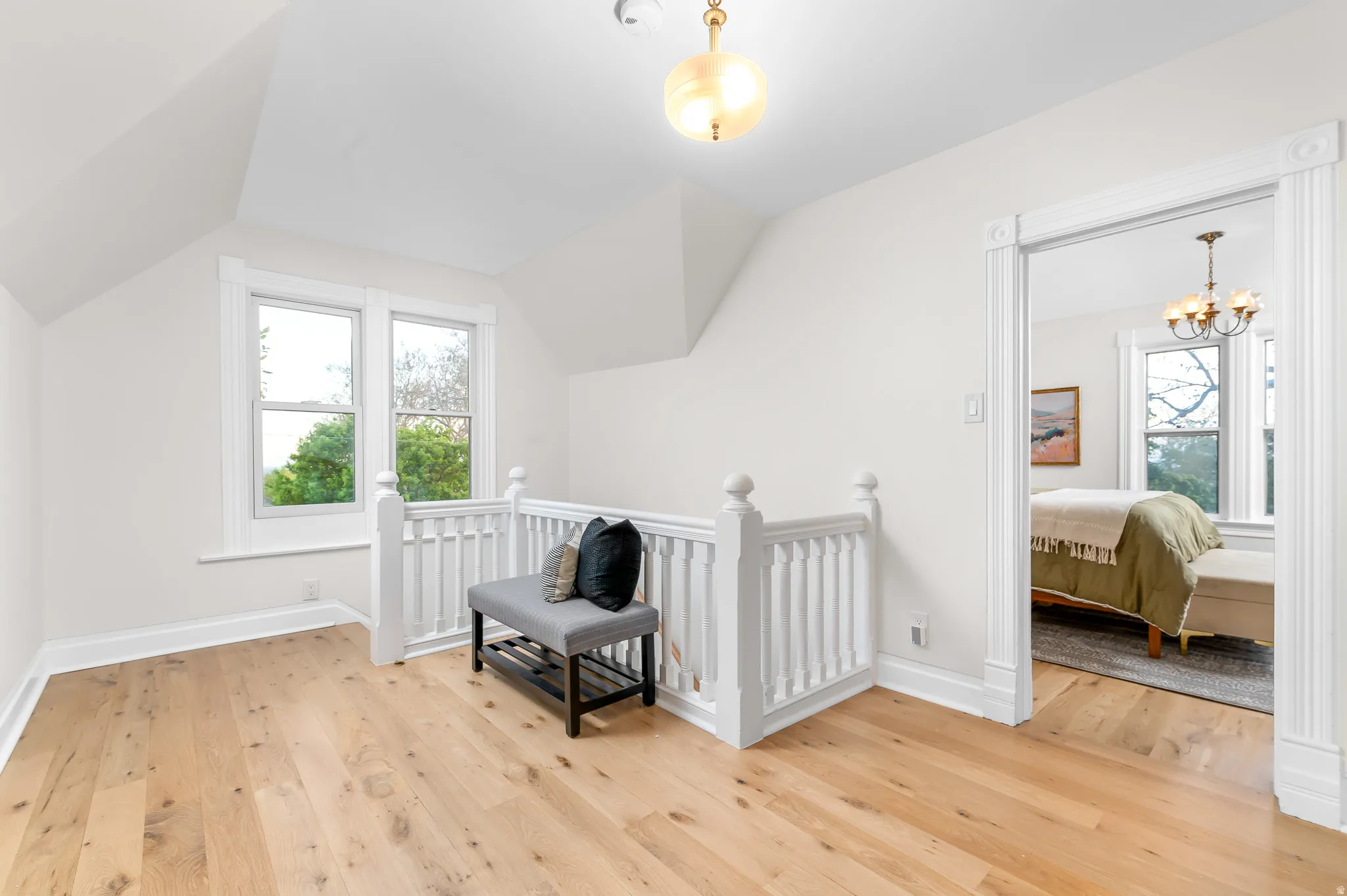 Upper-level landing featuring light wood-finish flooring, white painted walls, a white balustrade, two double-hung windows, and a decorative ceiling light fixture