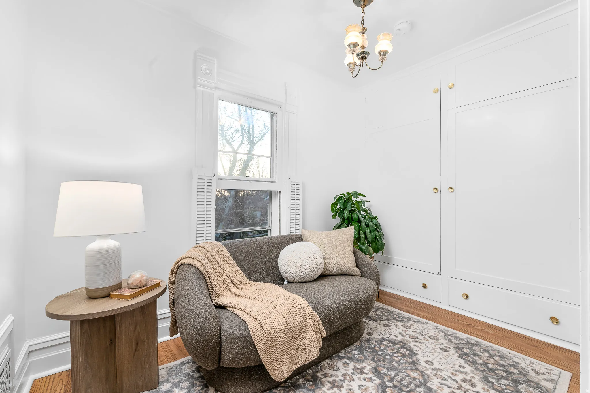 Built-in white cabinetry with brass knob hardware, wood-finish flooring, white window shutters, and a brass chandelier