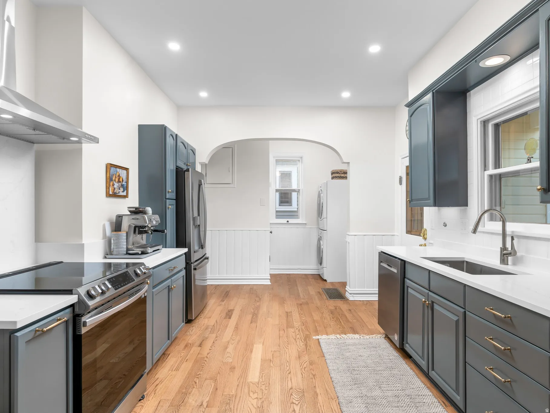 Modern kitchen featuring stainless steel appliances, dark cabinetry with brass-finish hardware, light countertops, and wood-finish flooring