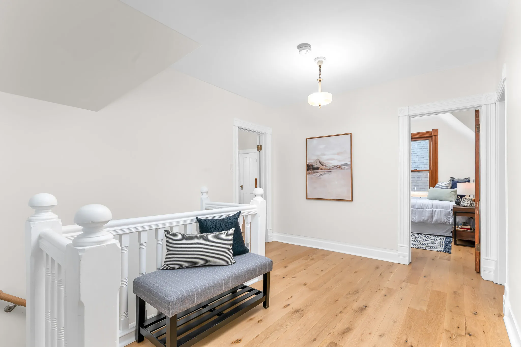 Hardwood flooring throughout a light-filled hallway, featuring a white painted balustrade and a flush-mount ceiling light fixture