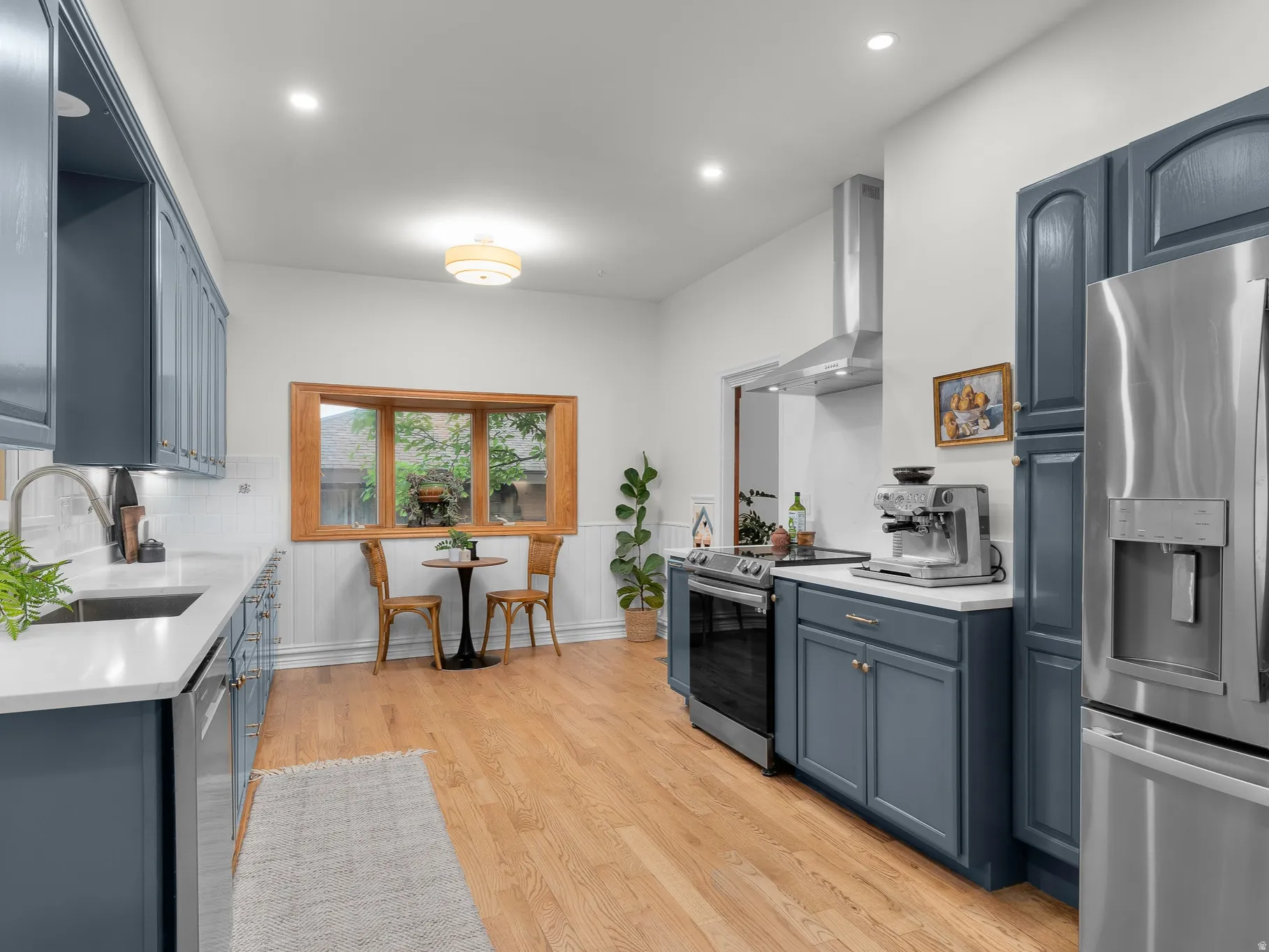 Modern kitchen featuring blue cabinetry, white countertops, stainless steel appliances, wood-finish flooring, and a bay window