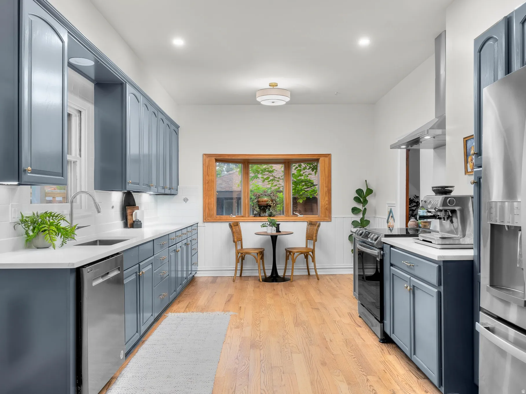 Kitchen featuring blue cabinetry, light countertops, wood-finish flooring, stainless steel appliances, and a wood-framed window