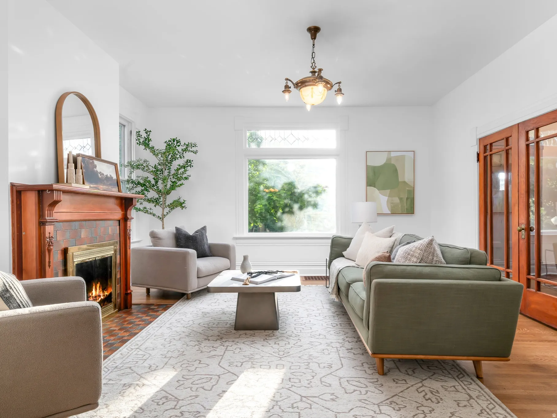 Living room featuring a detailed wood fireplace mantel with tiled surround, large windows providing natural light, hardwood flooring, and French doors with glass panes