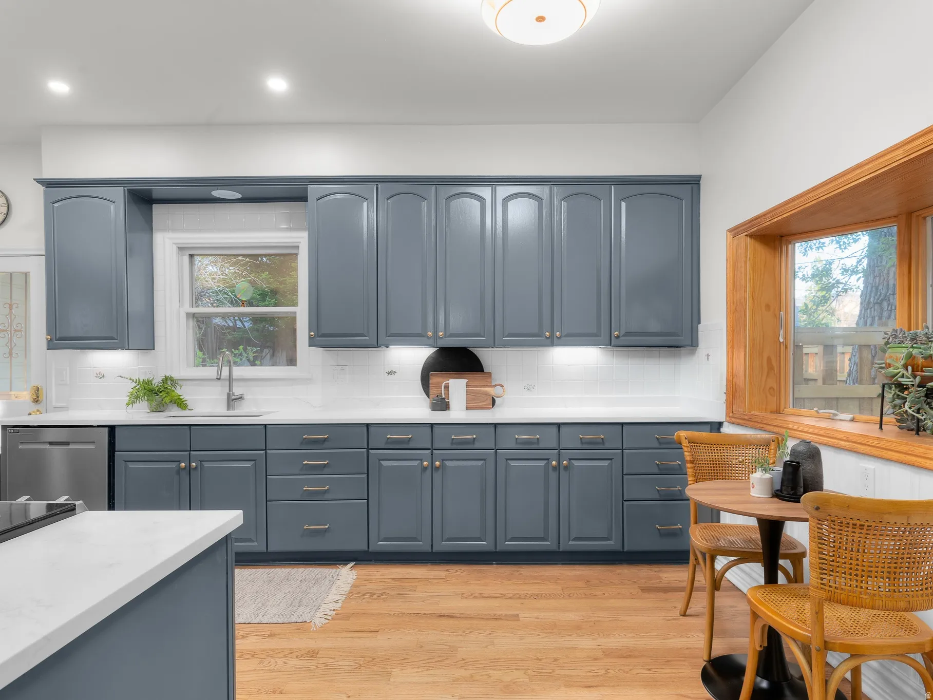 Kitchen featuring blue shaker cabinetry, white countertops, stainless steel dishwasher, white subway tile backsplash, and wood-finish flooring
