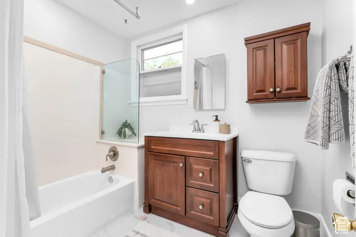 Bathroom featuring a built-in bathtub with a glass partition, wood-finish vanity with countertop sink, wall-mounted mirror, and a window providing natural light