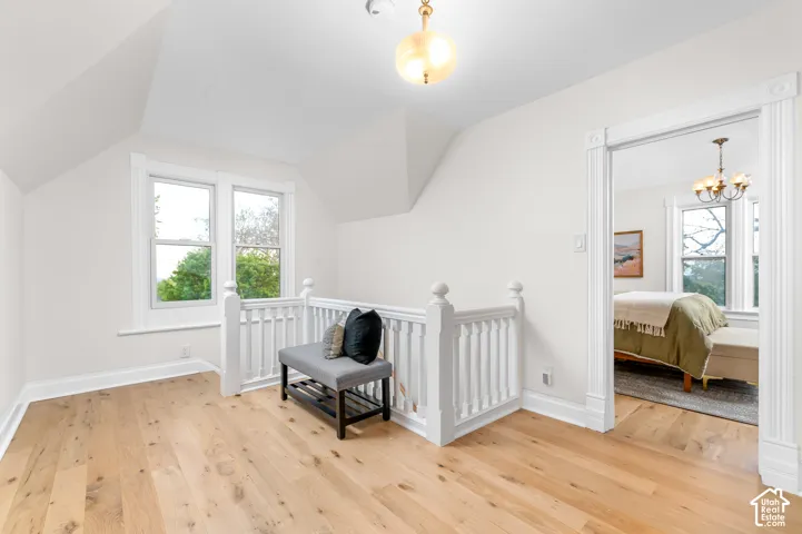 Upper-level landing featuring light wood-finish flooring, white painted walls, a white balustrade, two double-hung windows, and a decorative ceiling light fixture