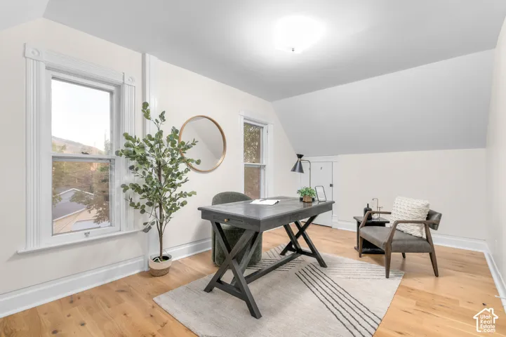 Room featuring wood-finish flooring, white walls, two windows with decorative trim, and a sloped ceiling