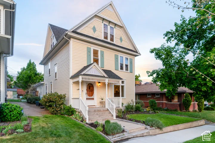 Clapboard siding exterior with a pitched roof, decorative gable details, covered front porch, and a landscaped front yard with mature plantings