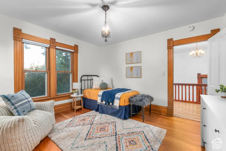 Hardwood flooring, ornate wood window trim, decorative ceiling light fixture, white interior walls, and an open doorway with wood trim