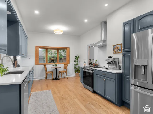 Modern kitchen featuring blue cabinetry, white countertops, stainless steel appliances, wood-finish flooring, and a bay window