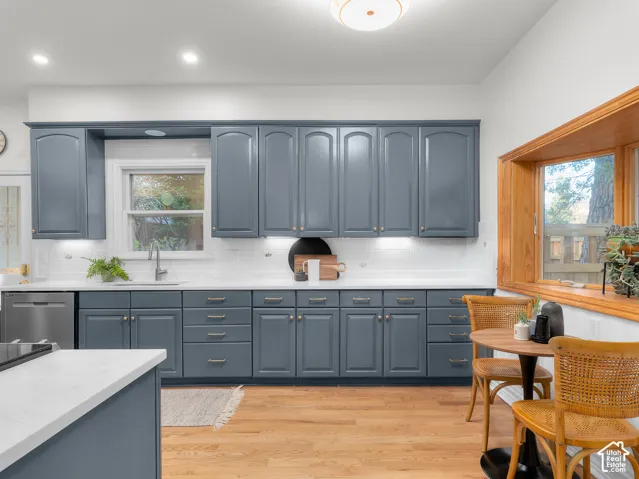 Kitchen featuring blue shaker cabinetry, white countertops, stainless steel dishwasher, white subway tile backsplash, and wood-finish flooring