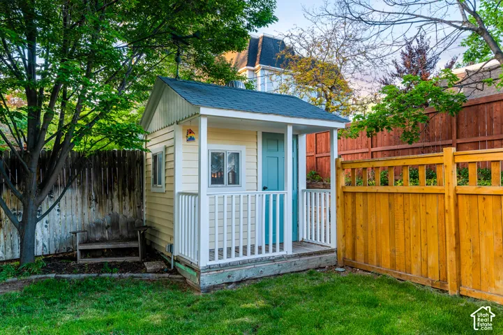 Backyard structure featuring a pitched roof, yellow siding, and a covered porch with white railings