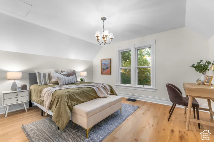 Sloped ceilings with a chandelier, wood-finish flooring, and white trim around a double window