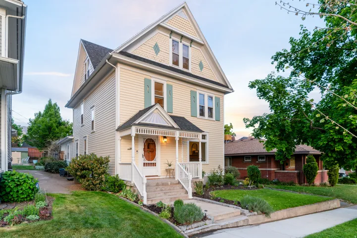 Clapboard siding exterior with a pitched roof, decorative gable details, covered front porch, and a landscaped front yard with mature plantings