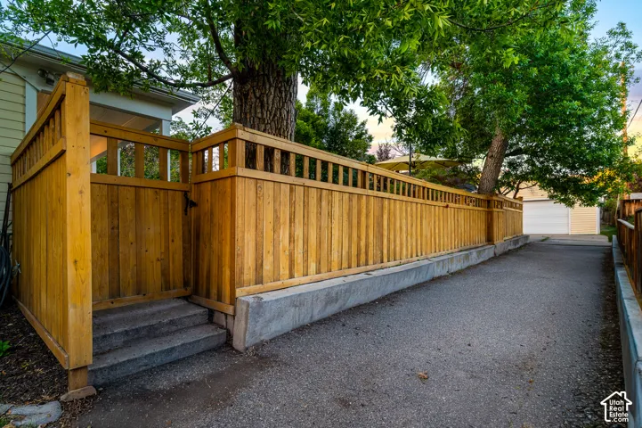 Paved driveway bordered by a wood privacy fence on a concrete base, featuring a gated entrance with steps and mature trees