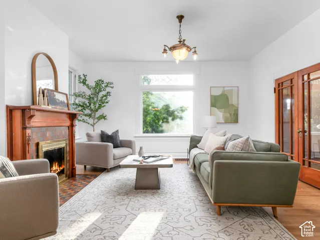 Living room featuring a detailed wood fireplace mantel with tiled surround, large windows providing natural light, hardwood flooring, and French doors with glass panes