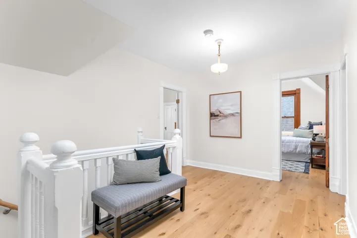 Hardwood flooring throughout a light-filled hallway, featuring a white painted balustrade and a flush-mount ceiling light fixture