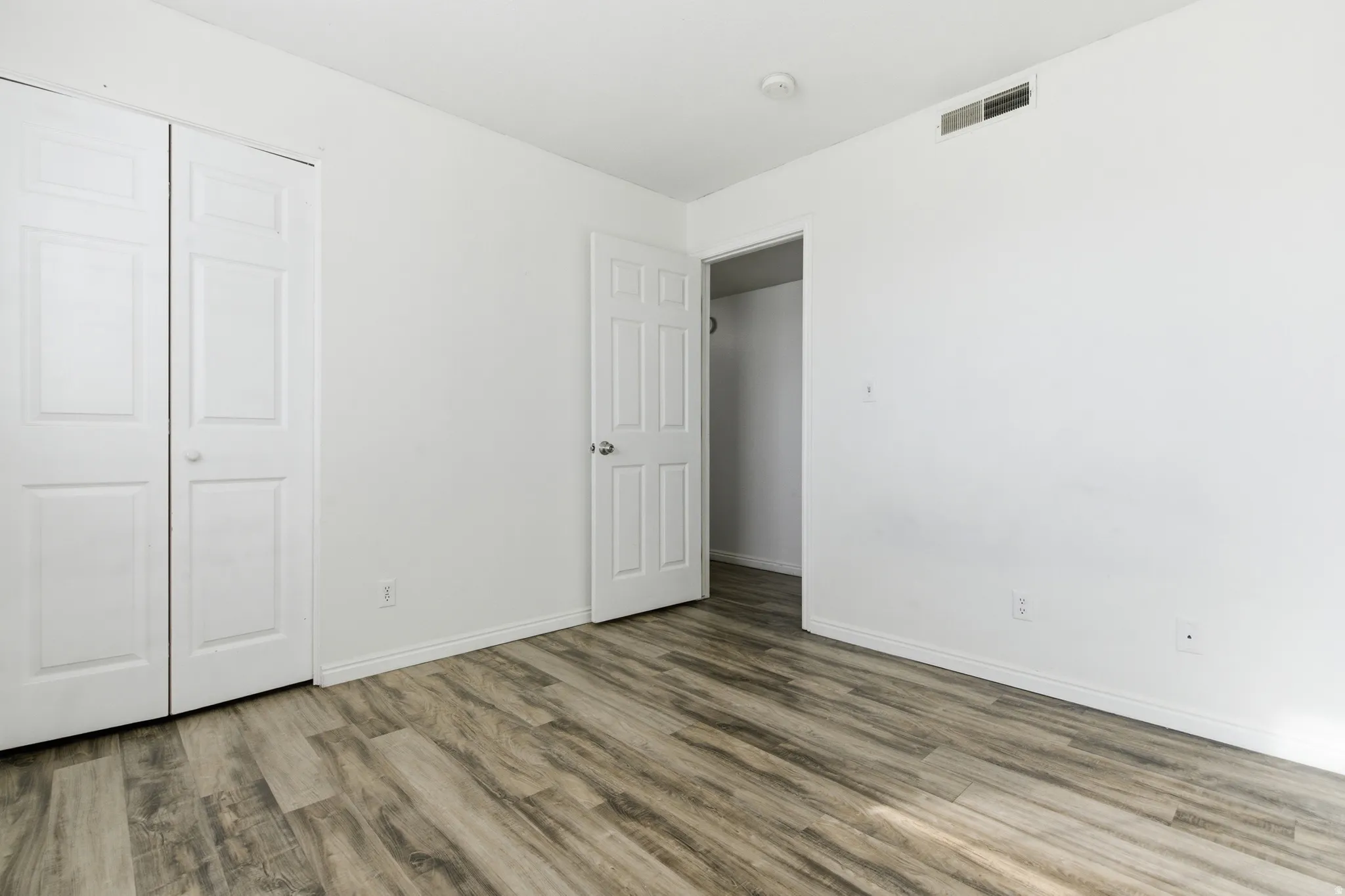 Spacious room featuring wood-finish flooring, white baseboards, and bright white walls