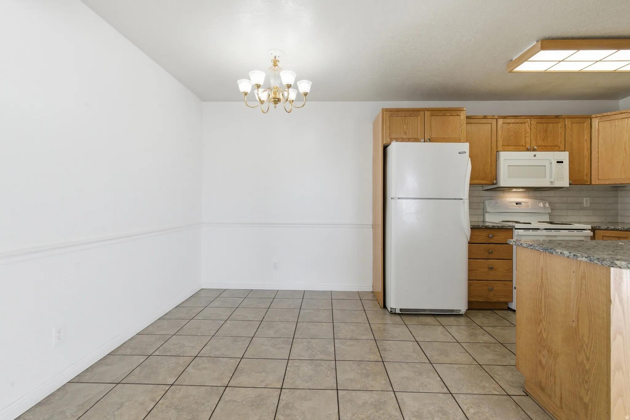 Kitchen and dining area featuring light wood cabinetry, white appliances, a tiled backsplash, and granite countertops