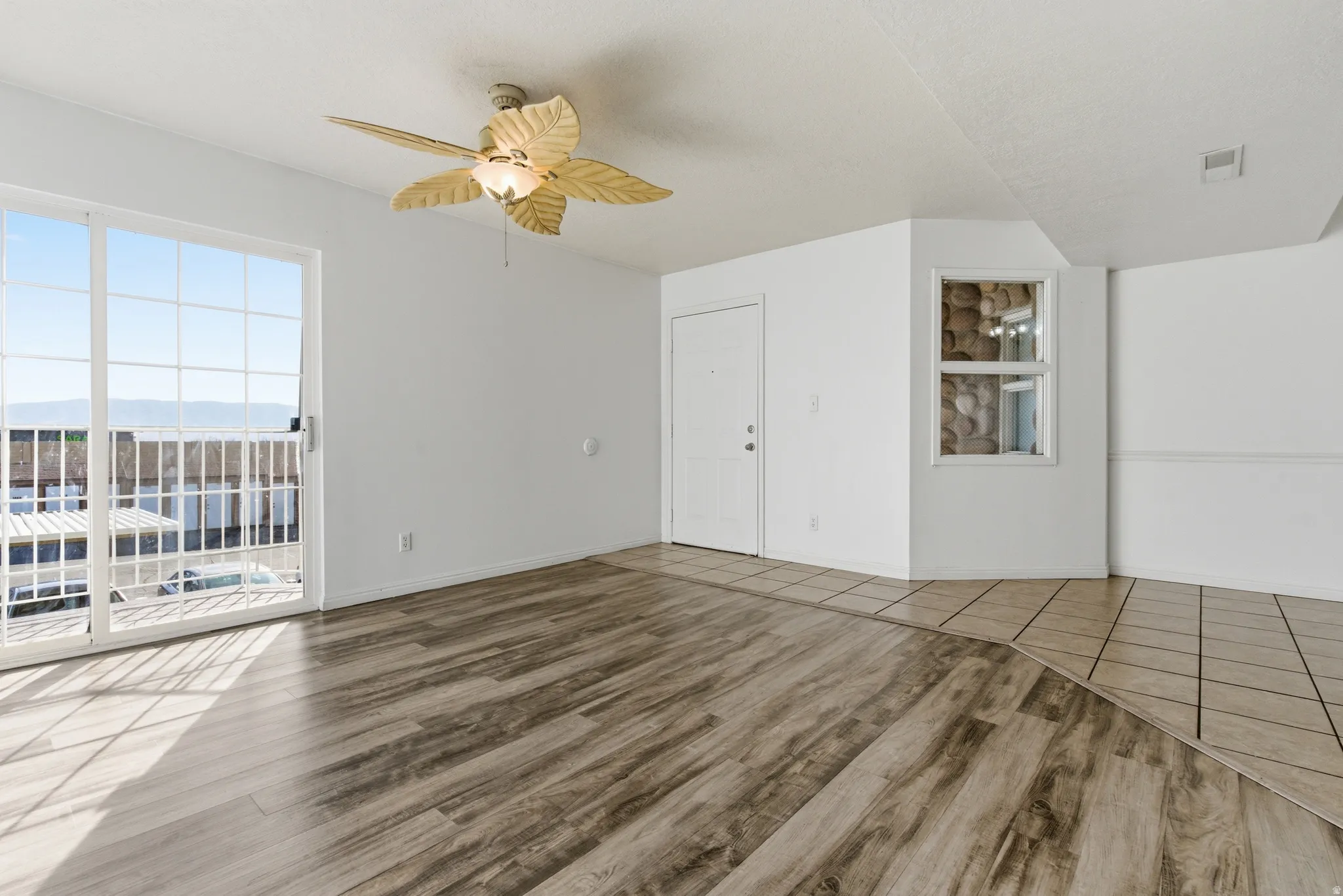 Open living area featuring wood-finish flooring, a ceiling fan with integrated lighting, and a sliding glass door leading to a balcony