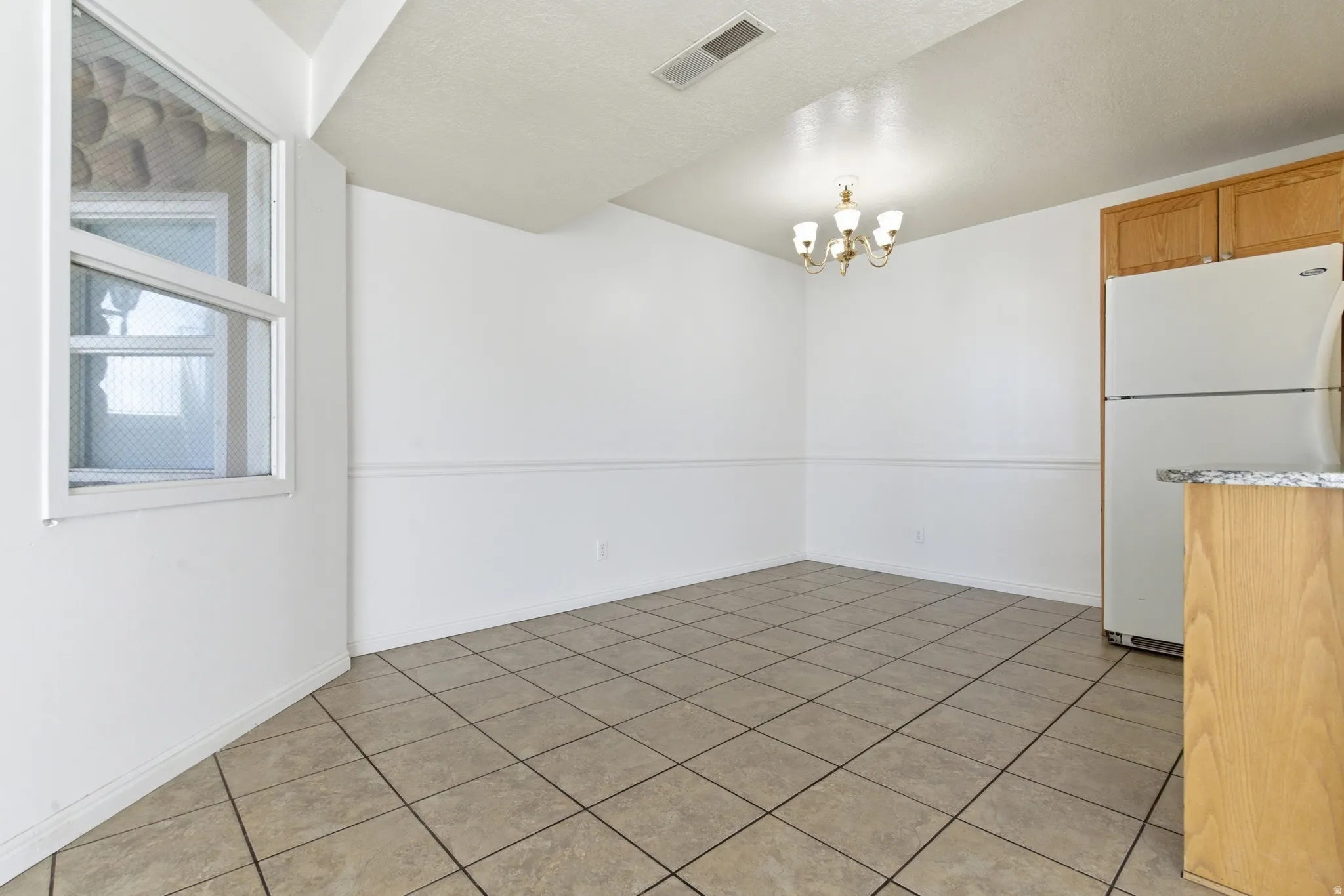 Dining area featuring tiled flooring, a traditional chandelier, baseboard and chair rail molding, and a window with a textured glass panel