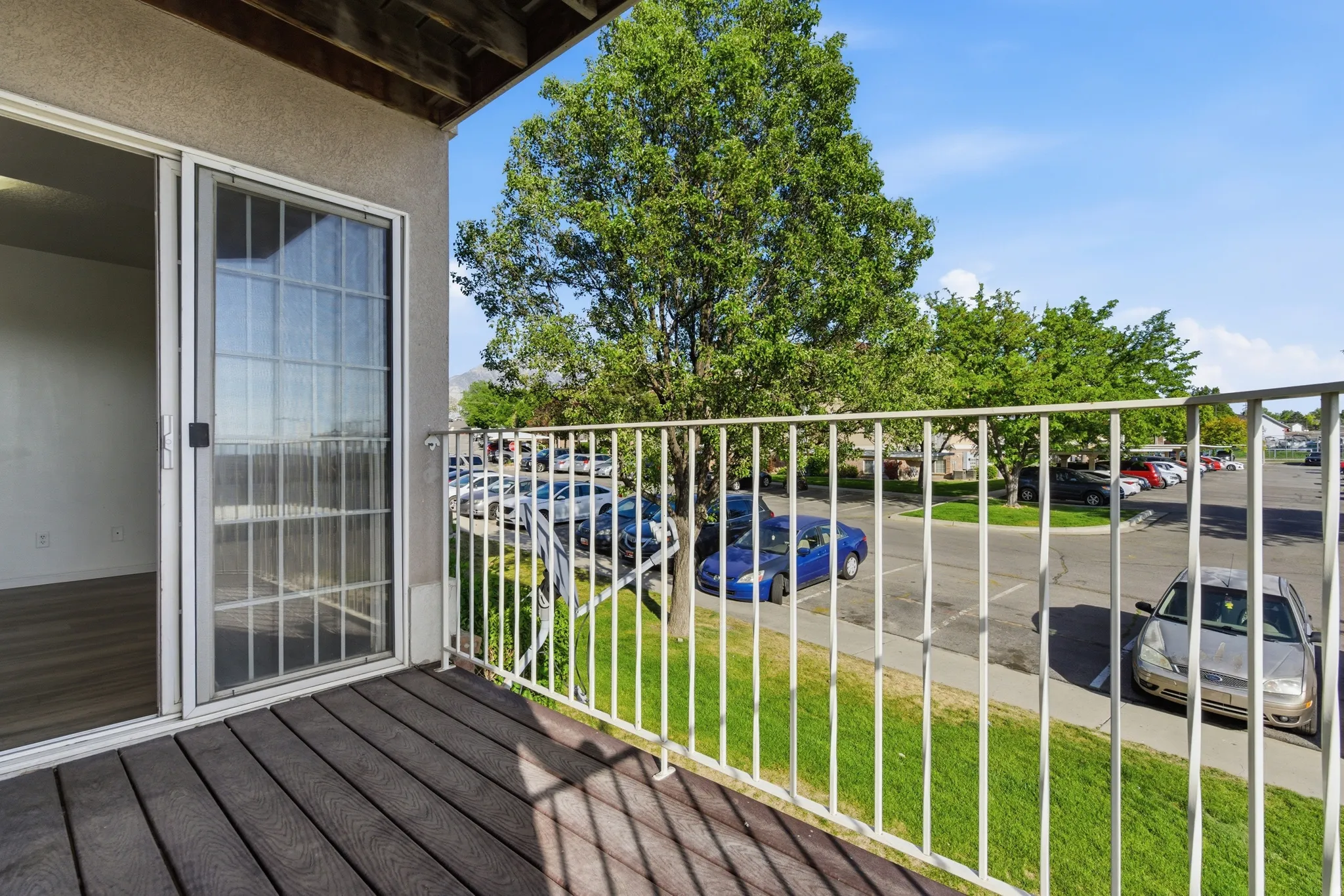 Private balcony with composite decking and white railing, featuring sliding glass door access to the interior space with wood-finish flooring