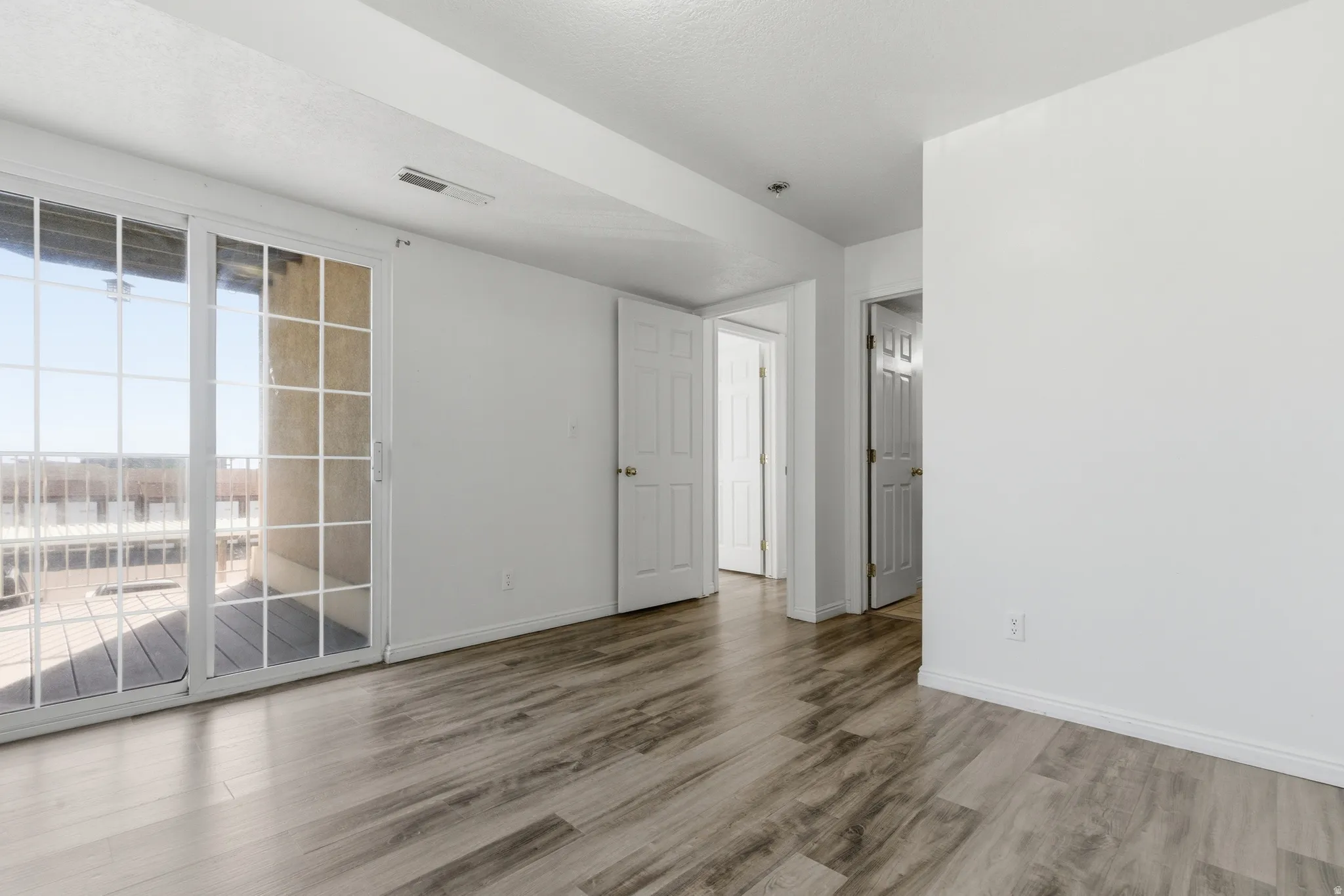 Expansive room featuring wood-finish flooring, white walls, and a large sliding glass door
