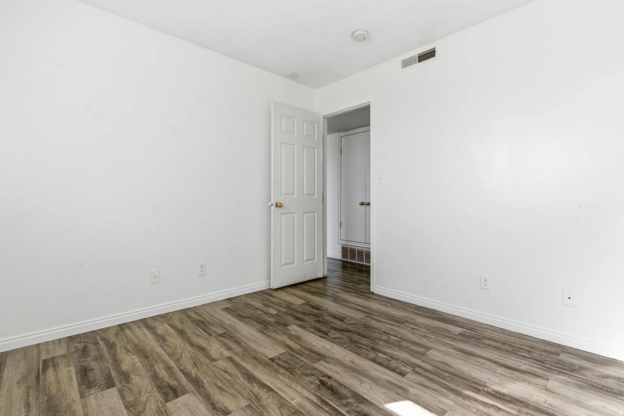 Spacious room featuring wood-finish flooring, white baseboards, and bright white walls