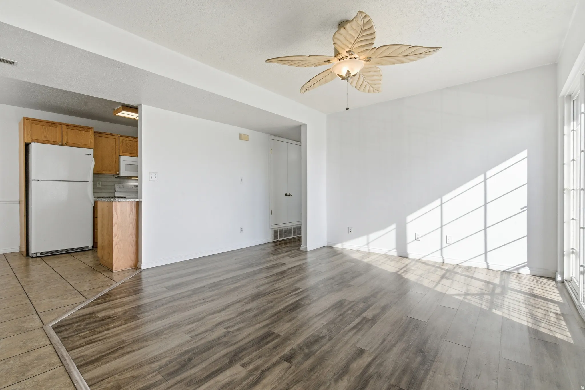 Spacious living area featuring wood-finish flooring, a decorative ceiling fan, and sliding glass doors