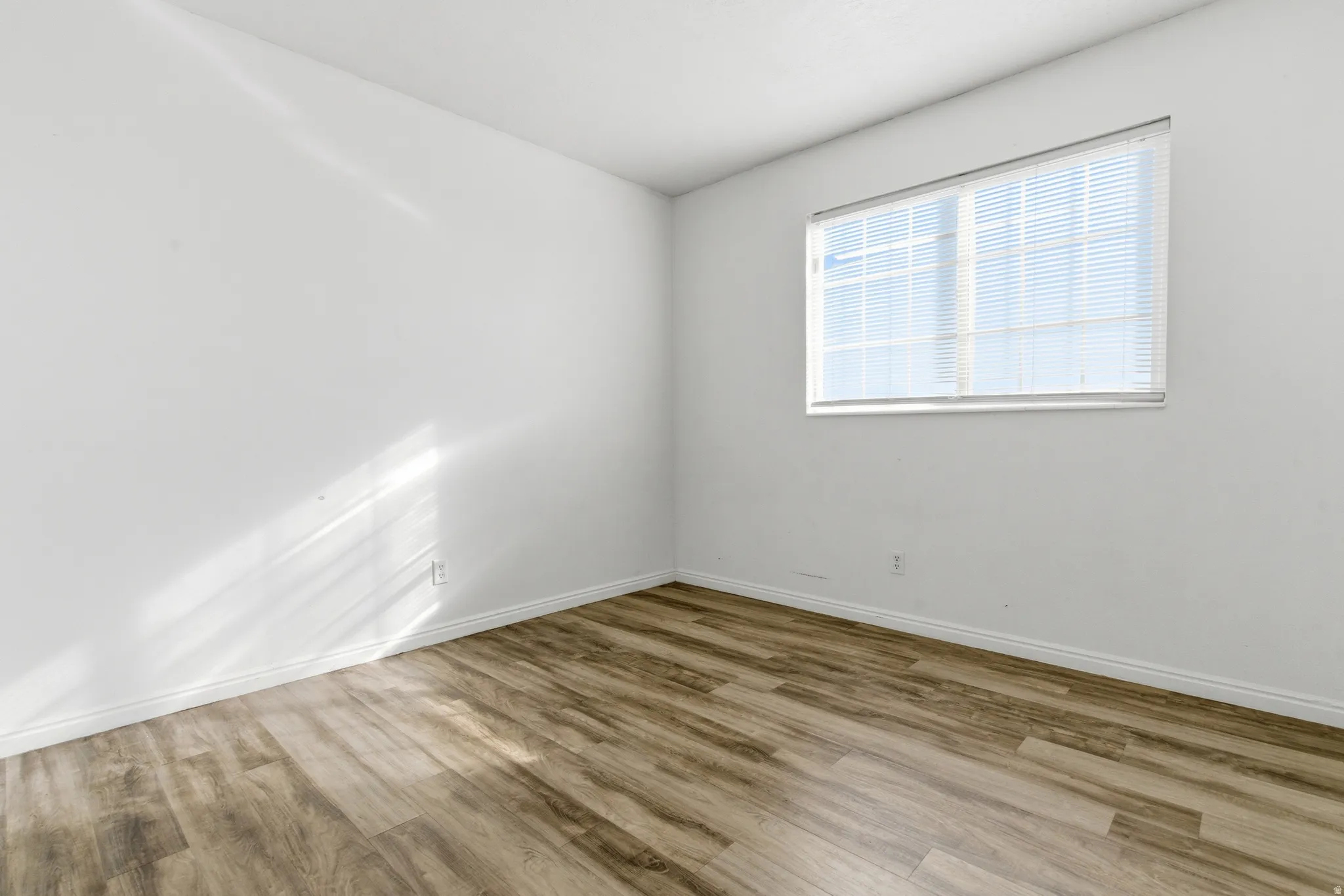 Room featuring wood-finish flooring, white baseboards, and a window with horizontal blinds