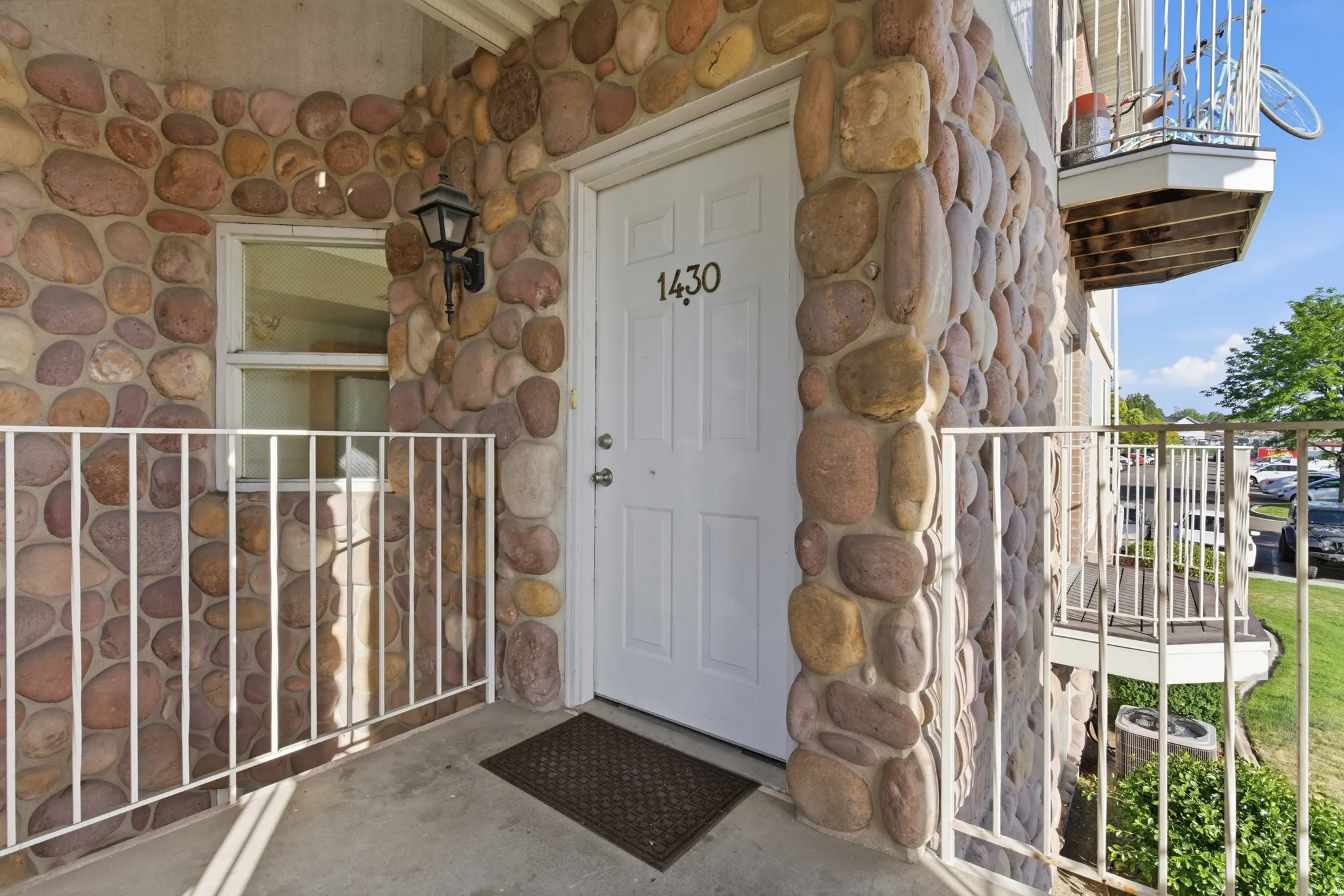 Entryway featuring a white door with black numerals, an exterior wall with natural stone facing, a white railing, and an outdoor wall lantern