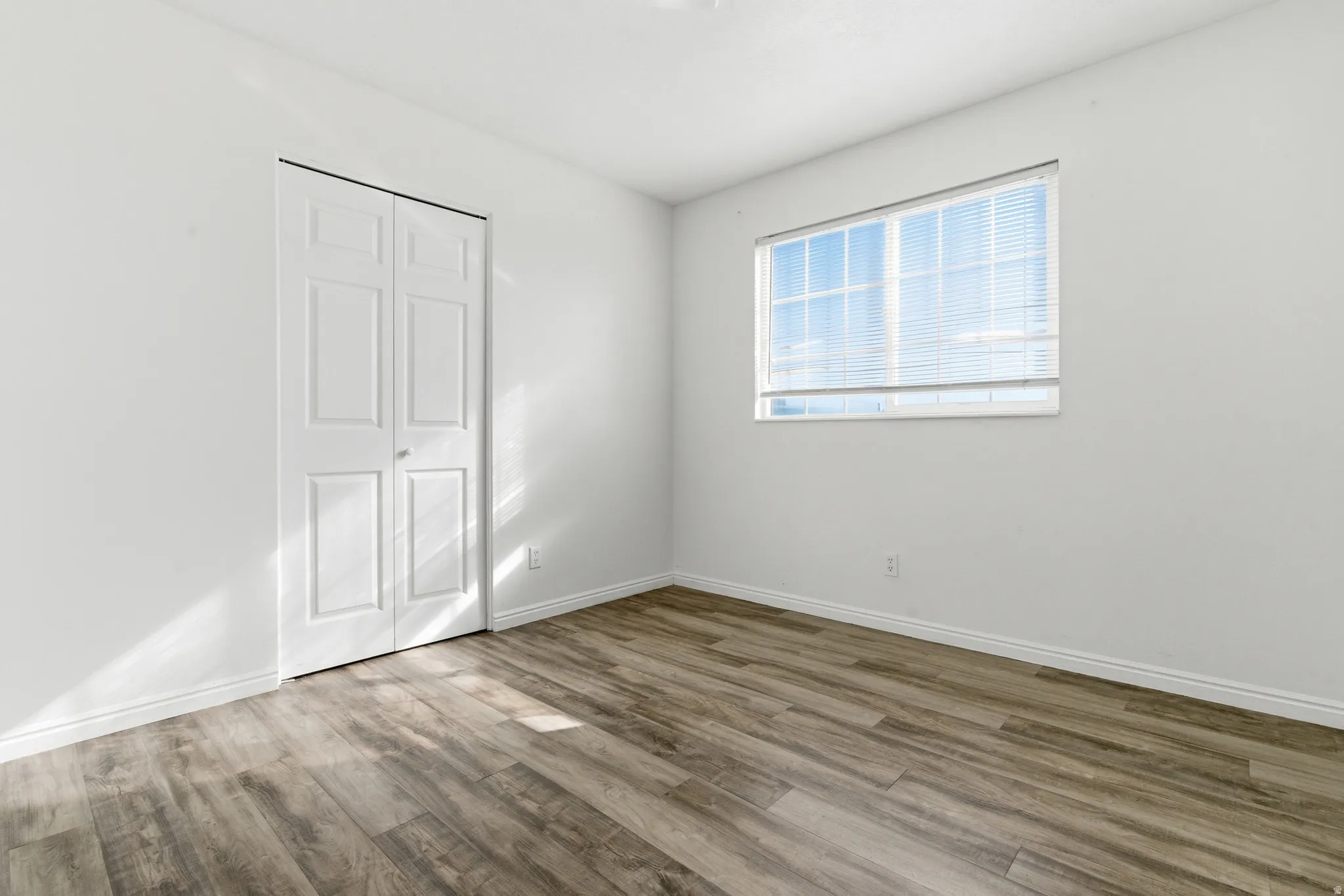 Room featuring wood-finish flooring, white baseboards, and a bi-fold closet door