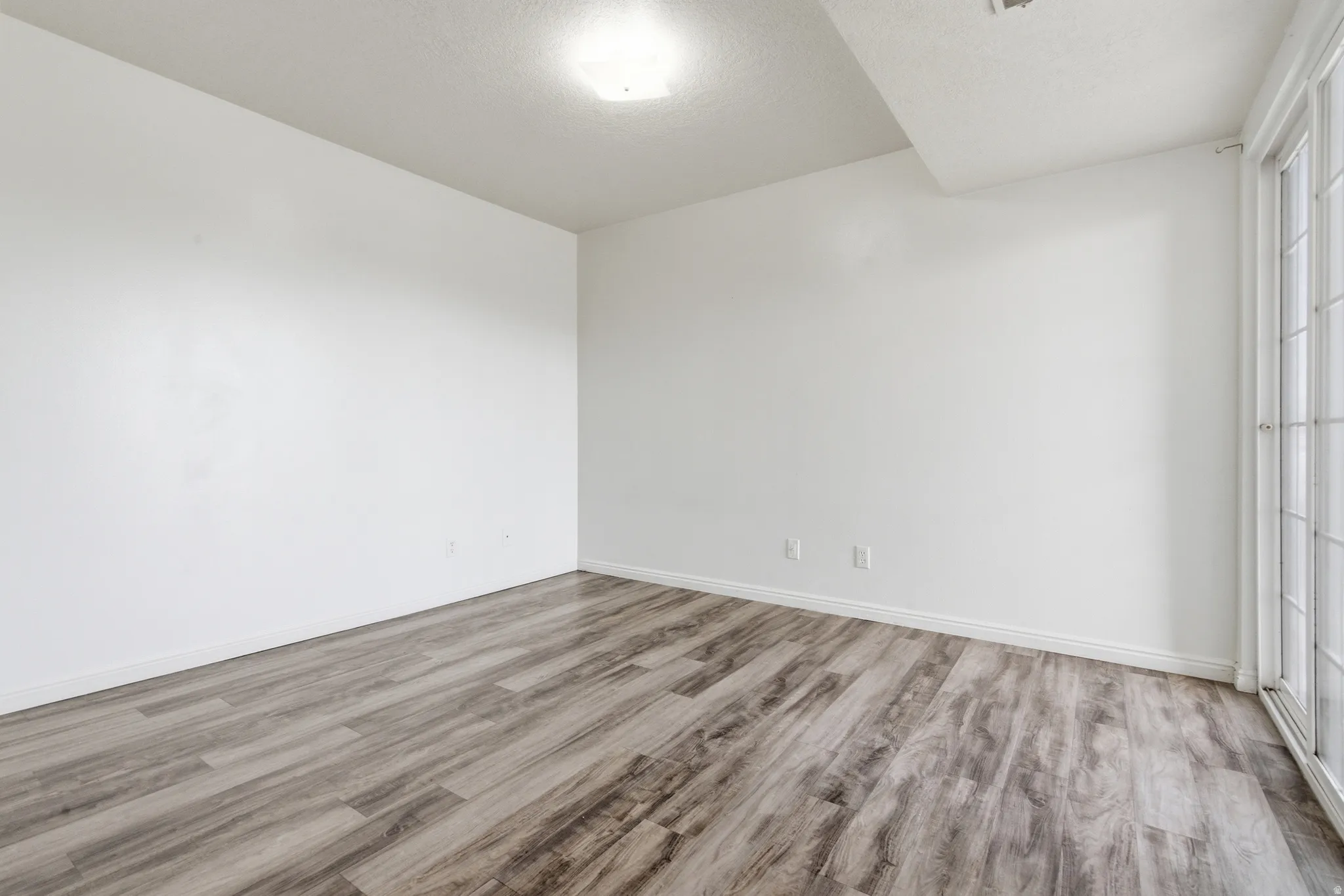Spacious room featuring wood-finish flooring, white baseboards, and bright white walls