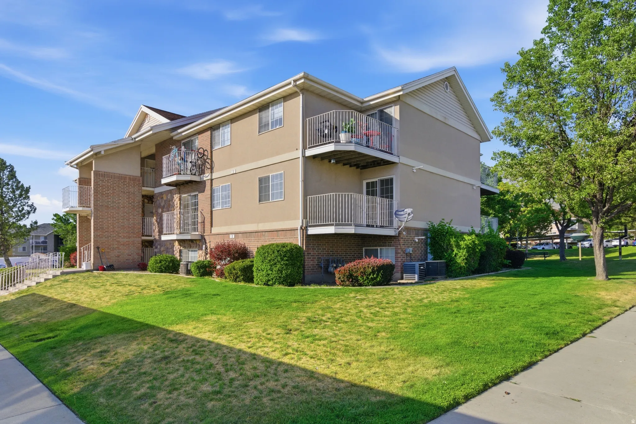 Multi-story residential building featuring balconies with white railings, a tan stucco exterior, and brick accents