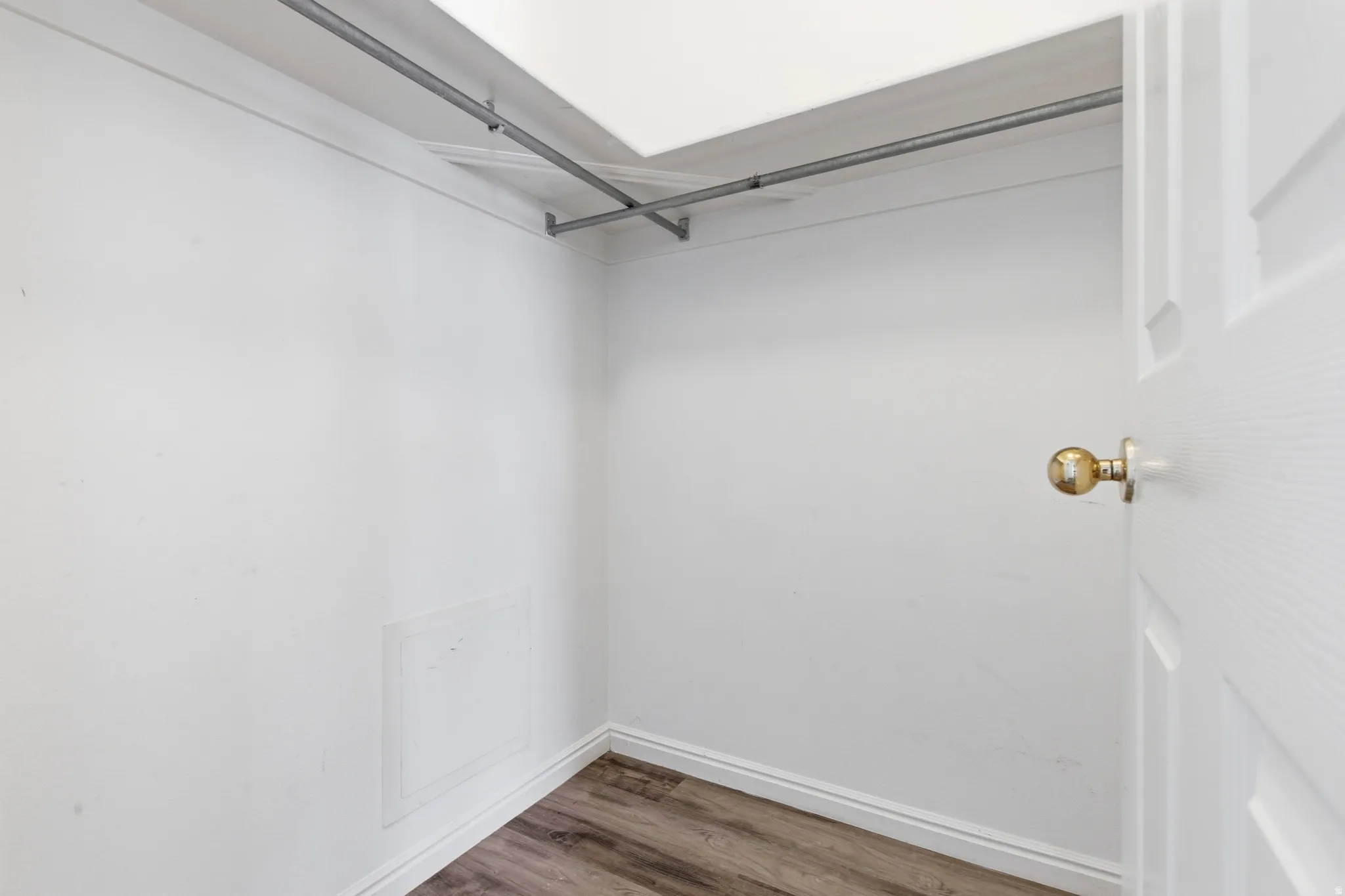 Interior closet featuring wood-finish flooring, white baseboards, and a metal hanging rod