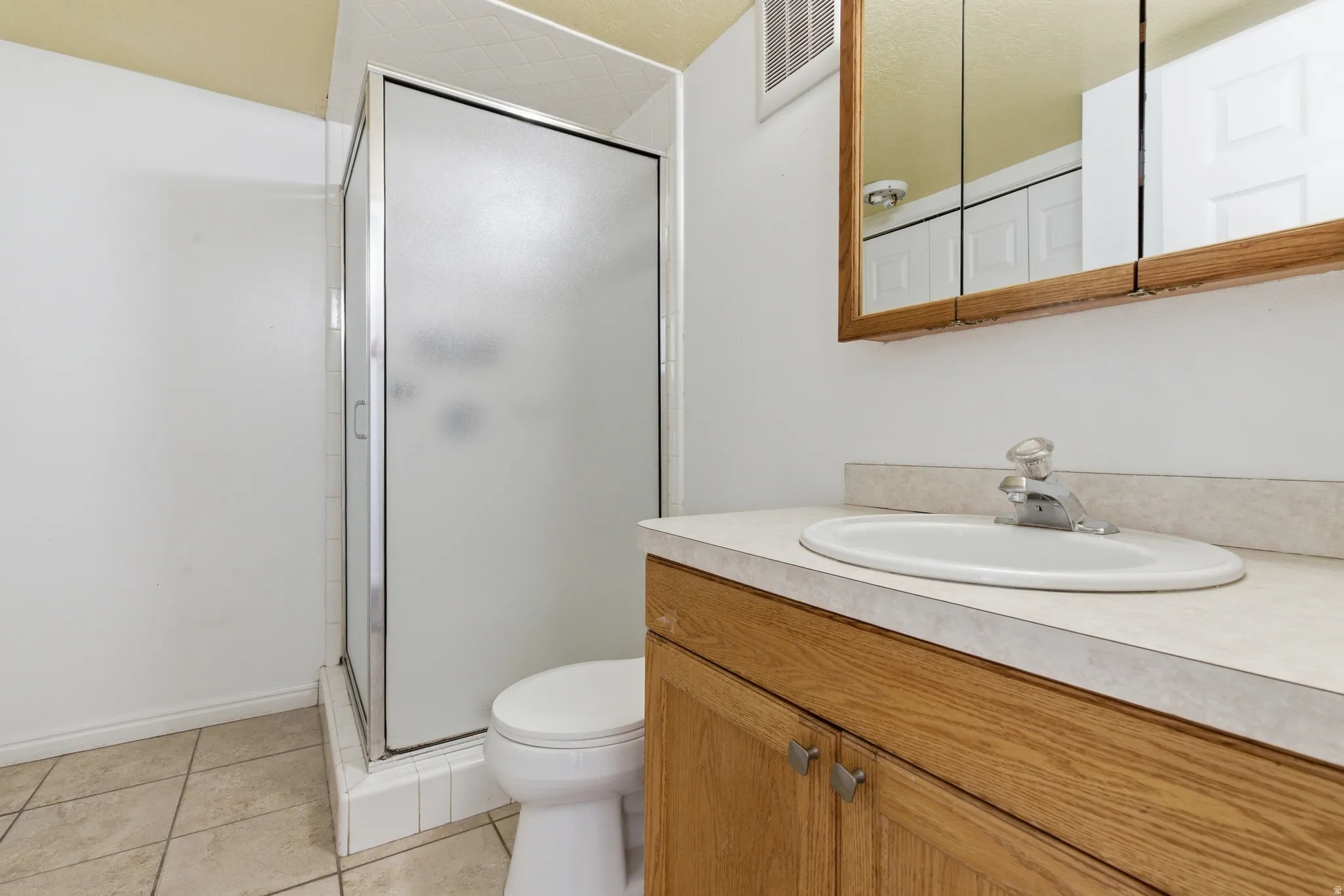 Bathroom featuring a frosted glass shower enclosure, a vanity with wood-finish cabinetry, a white oval sink, and a light-toned countertop
