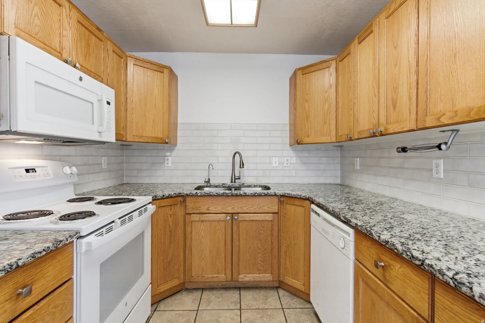 Kitchen featuring light wood cabinetry, white subway tile backsplash, and speckled countertops