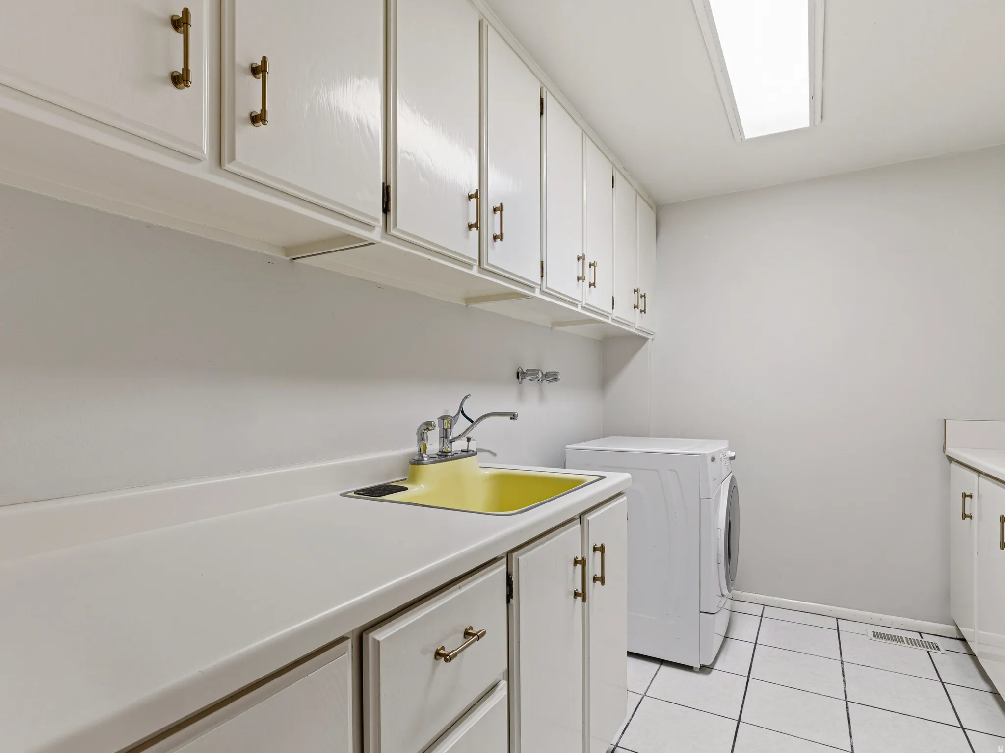 Utility area featuring white cabinetry with brass-toned hardware, extensive countertop space, a yellow utility sink with faucet, and white tiled flooring
