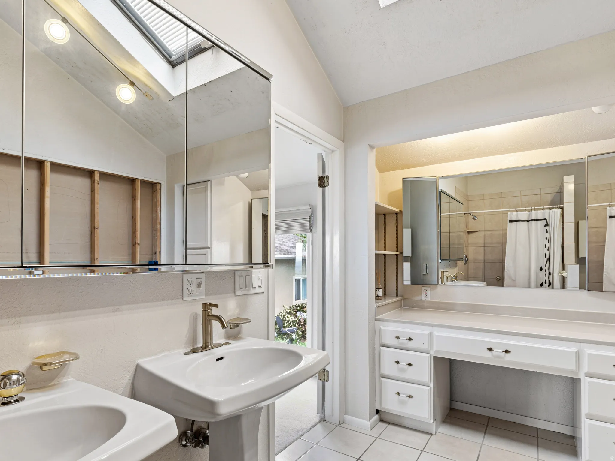 Bathroom featuring a pedestal sink, vanity with integrated cabinetry, tile flooring, and a skylight