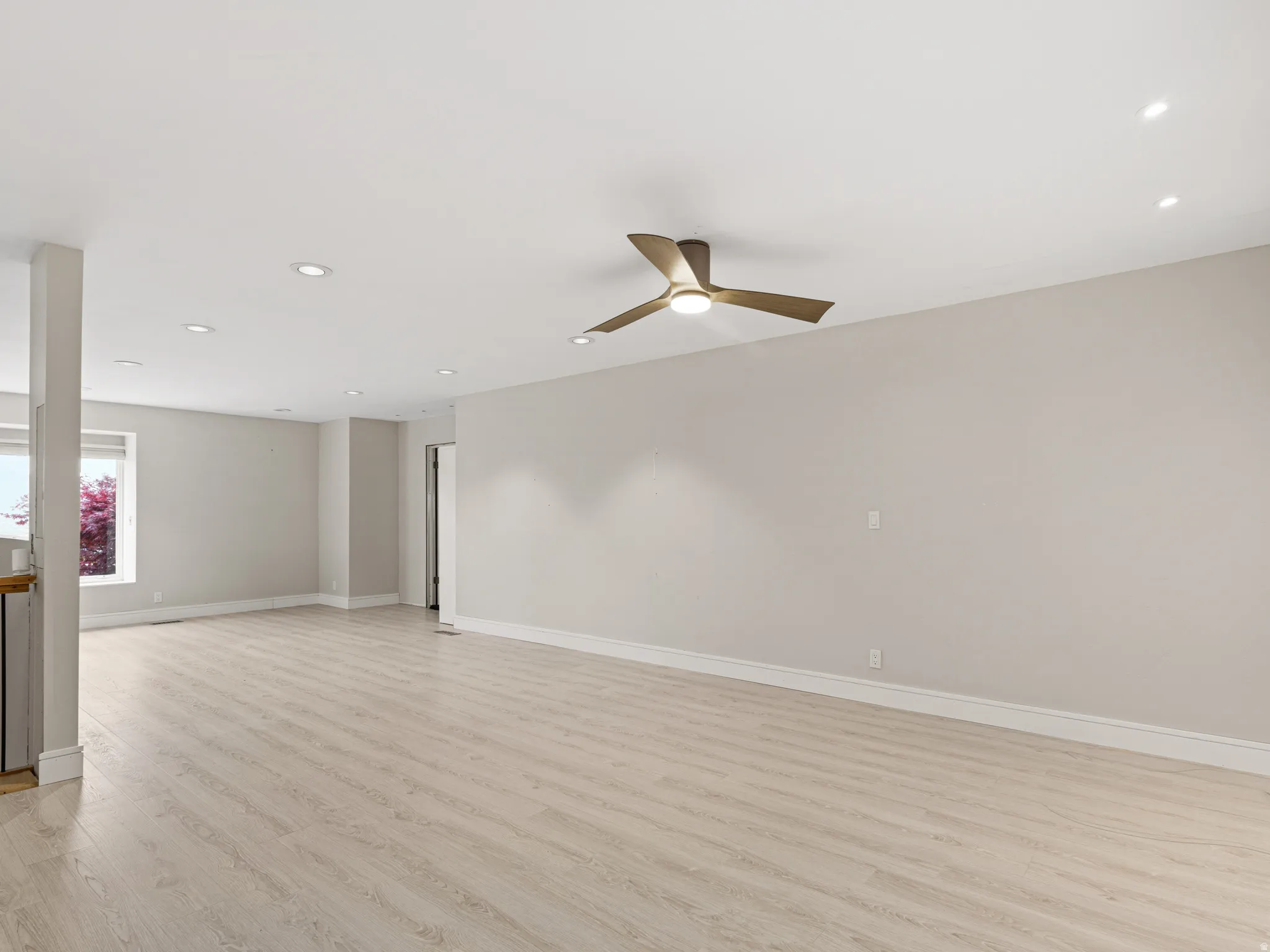 Spacious room with light wood-finish flooring, recessed lighting, and a modern ceiling fan